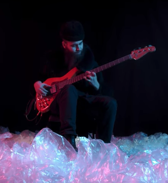 Cassius Lambert playing bass in a dark room and with the bass in his hands. 